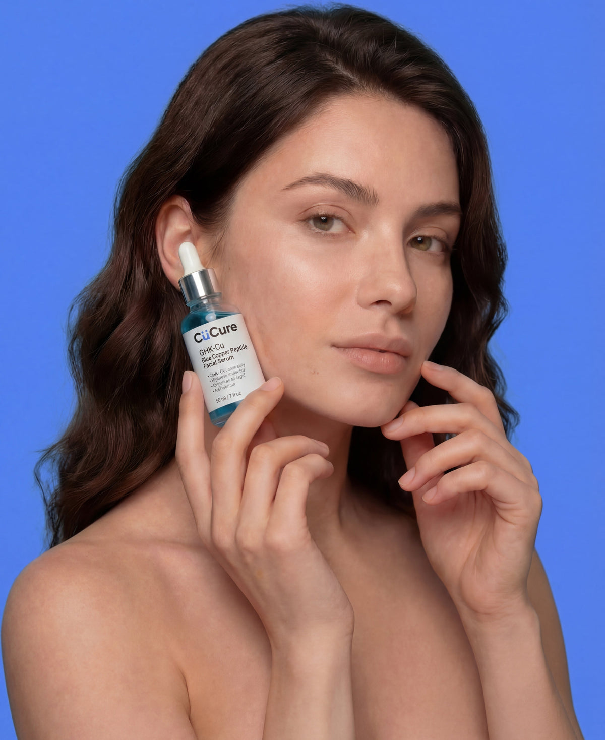 Woman holding a skincare serum bottle against a blue background